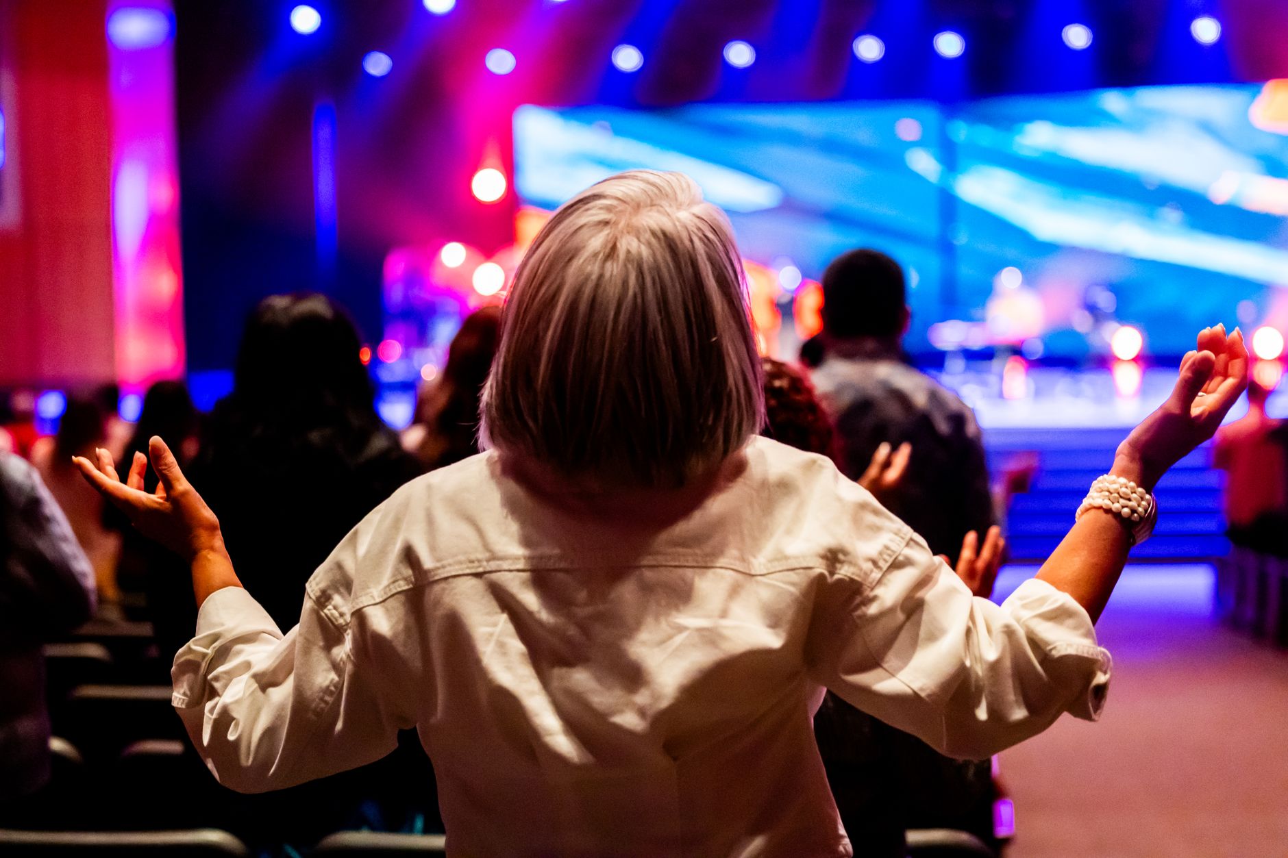 A vibrant indoor worship service with people raising hands in praise